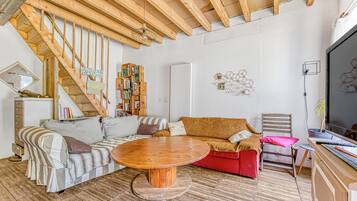 Un salon avec un escalier en bois, une table basse ronde en bois, un canapé, un fauteuil rouge et une bibliothèque.