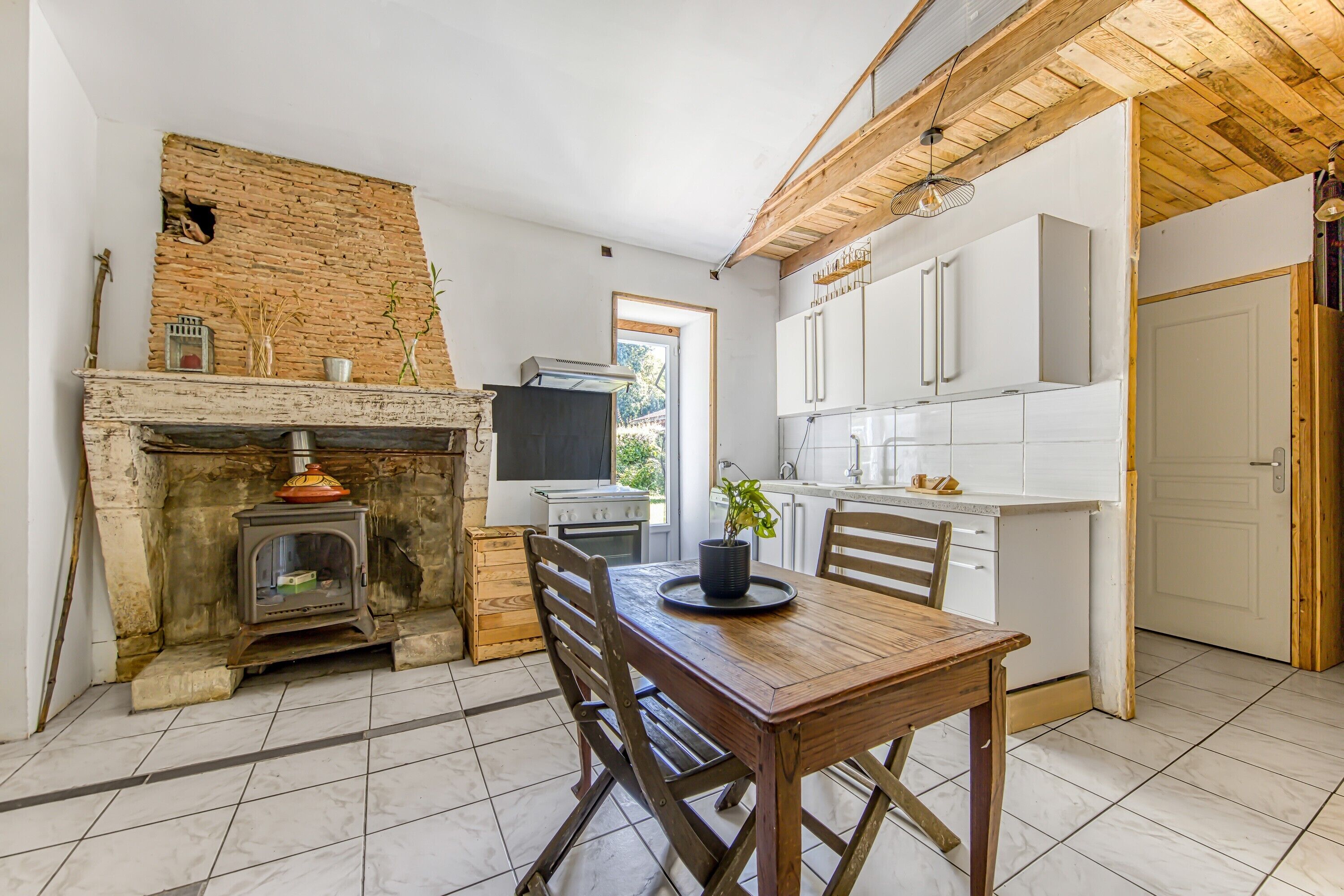 A kitchen with a brick wall, a wooden table, and a TV.