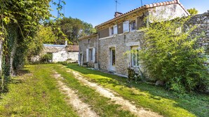 A stone building with a tiled roof, a dirt path, and surrounding greenery.