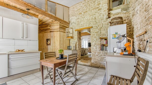 A rustic kitchen with wooden cabinets, a dining table with chairs, and a stone wall.