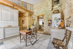 Une cuisine rustique avec des meubles de rangement en bois, une table à manger avec des chaises et un mur en pierre.