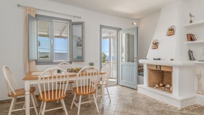 Un comedor con una mesa y sillas, una chimenea y vistas a través de un ventanal abierto.