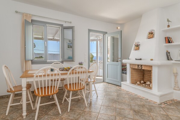 A dining area with a table and chairs, a fireplace, and a view through an open door.
