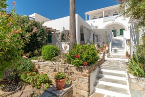 A white building with a stone staircase leading to a green door, surrounded by potted plants and greenery.