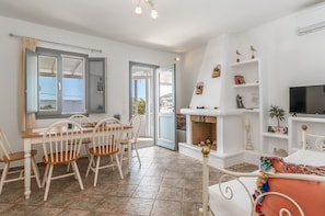 A room with a dining table, chairs, a fireplace, a TV, and a balcony with a view.