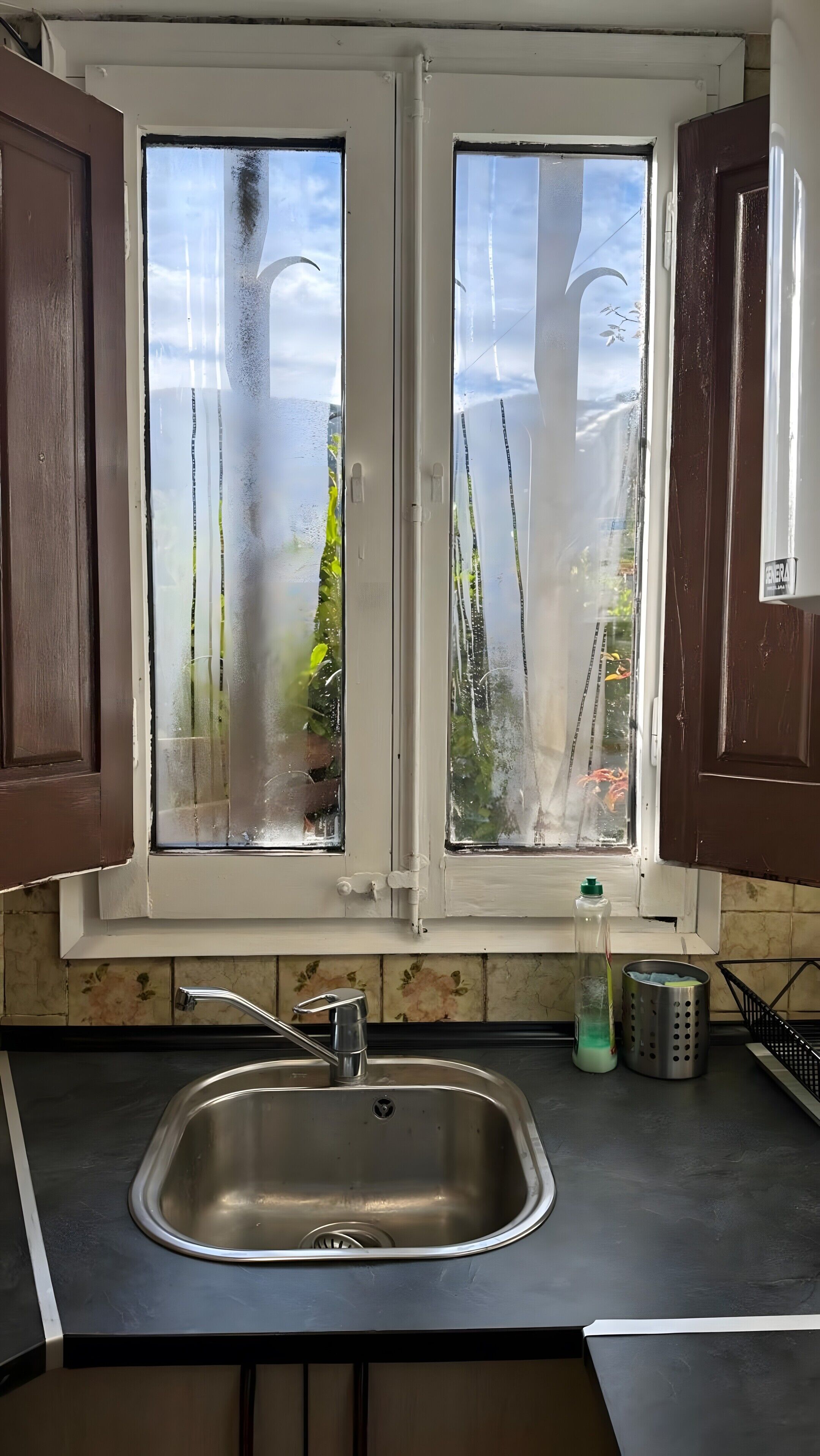Ett kök med en diskho i rostfritt stål, fönster med frostat glas och bruna skåp.
