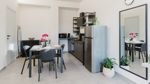 Uma cozinha moderna com geladeira, micro-ondas e armários. Há uma mesa de jantar com cadeiras e uma pequena ilha de cozinha.