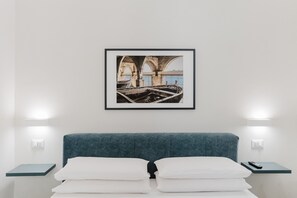 A hotel room with a bed, white pillows, a framed picture on the wall, and bedside lamps.
