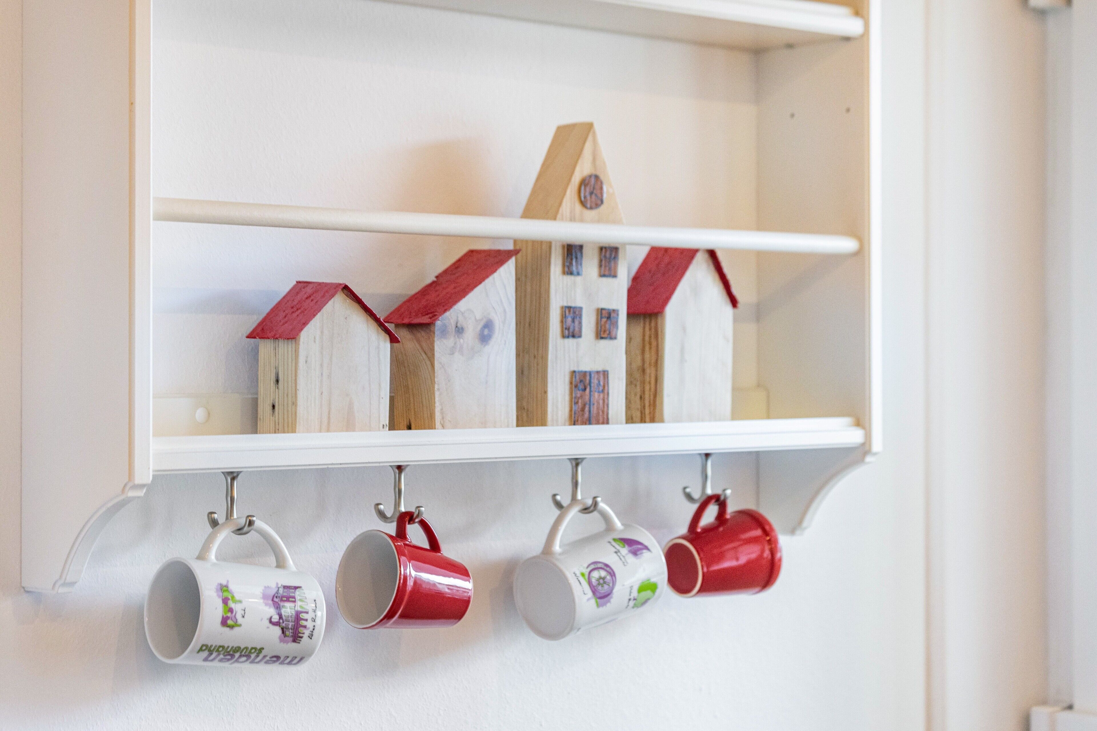 Een witte plank met houten modelhuisjes en mokken.