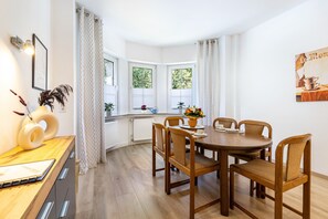 Un comedor con mesa y sillas de madera, una ventana con cortinas y un cuadro colgado en la pared.