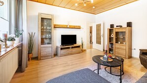 A modern living room with a wooden floor, a flat-screen TV, a coffee table, and a bookshelf.