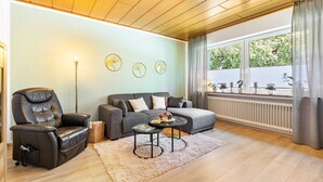 A living room with a leather recliner, a grey sofa, a coffee table, and a large window with curtains.