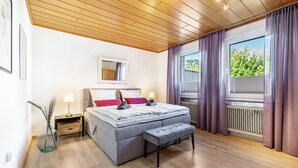 A bedroom with a bed, bedside tables, a mirror, a window with curtains, and a radiator.