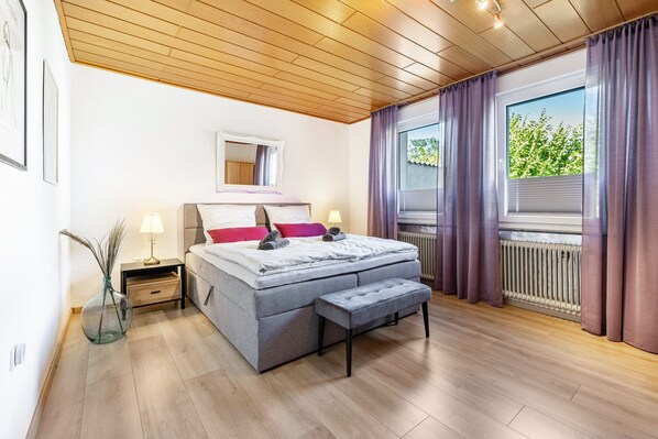 Un dormitorio con cama, mesitas de noche, un espejo, una ventana con cortinas y un radiador.