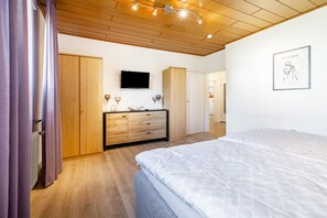 Un dormitorio con cama, armario de madera, cómoda y televisor montado en la pared.