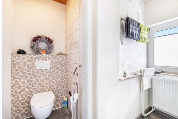 A bathroom with a toilet, shower, and a towel rack with towels.