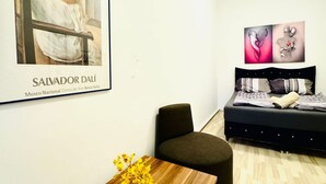 A modern room with a bed, a chair, a small table with flowers, and artwork on the wall.