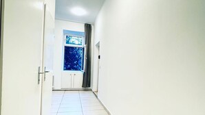 A hallway with white walls and a tiled floor, leading to a window with a view of trees.