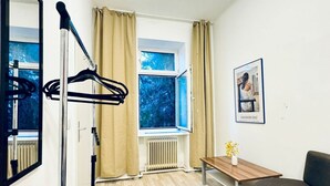 A room with a window, a radiator, a table with a vase, and a framed picture on the wall.