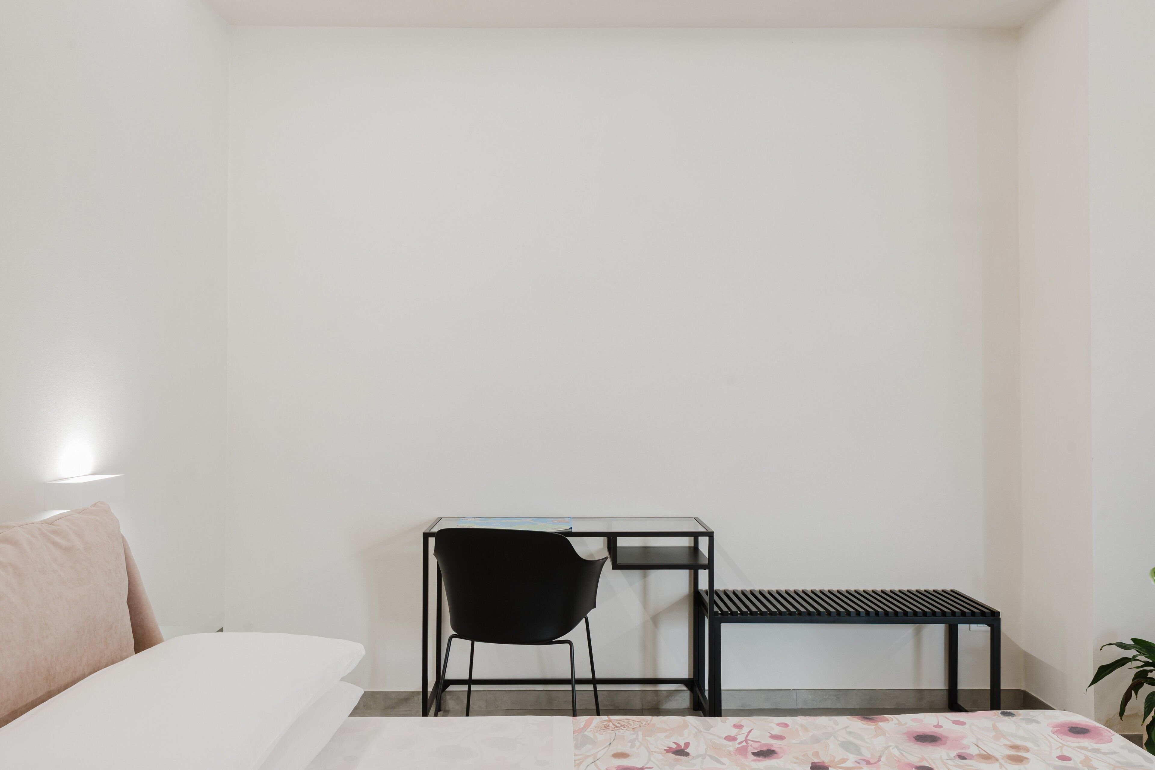 A minimalist room with a bed, a desk with a chair, and a small table.