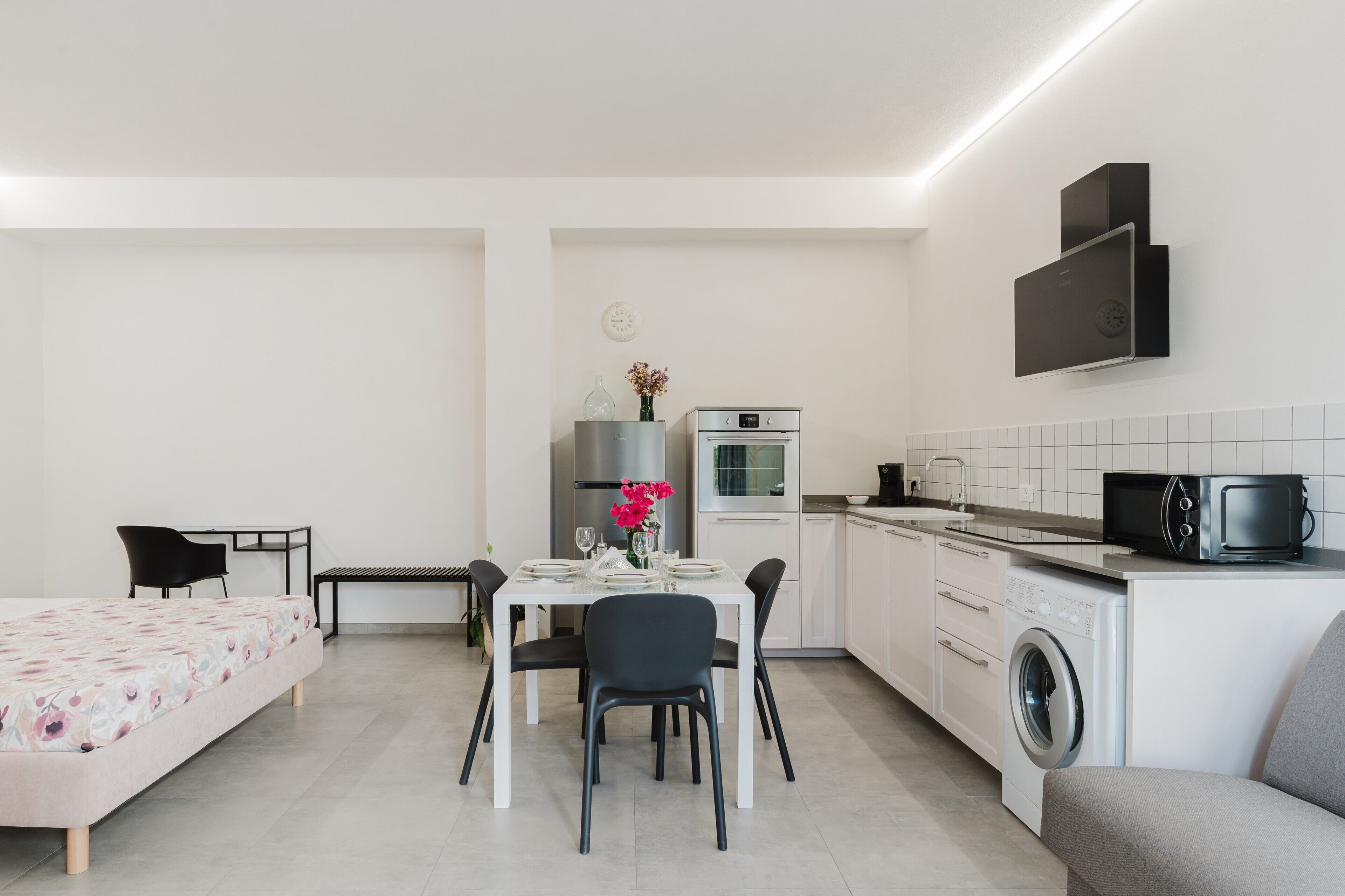 Una camera d'albergo compatta con un letto, un tavolo da pranzo con sedie, un angolo cottura con forno a microonde, una lavatrice e una piccola zona salotto con divano.