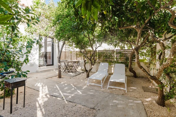 Une terrasse avec deux chaises longues blanches, une petite table et un barbecue.