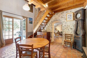 A rustic interior with a wooden dining table, chairs, a staircase, and a stone wall.