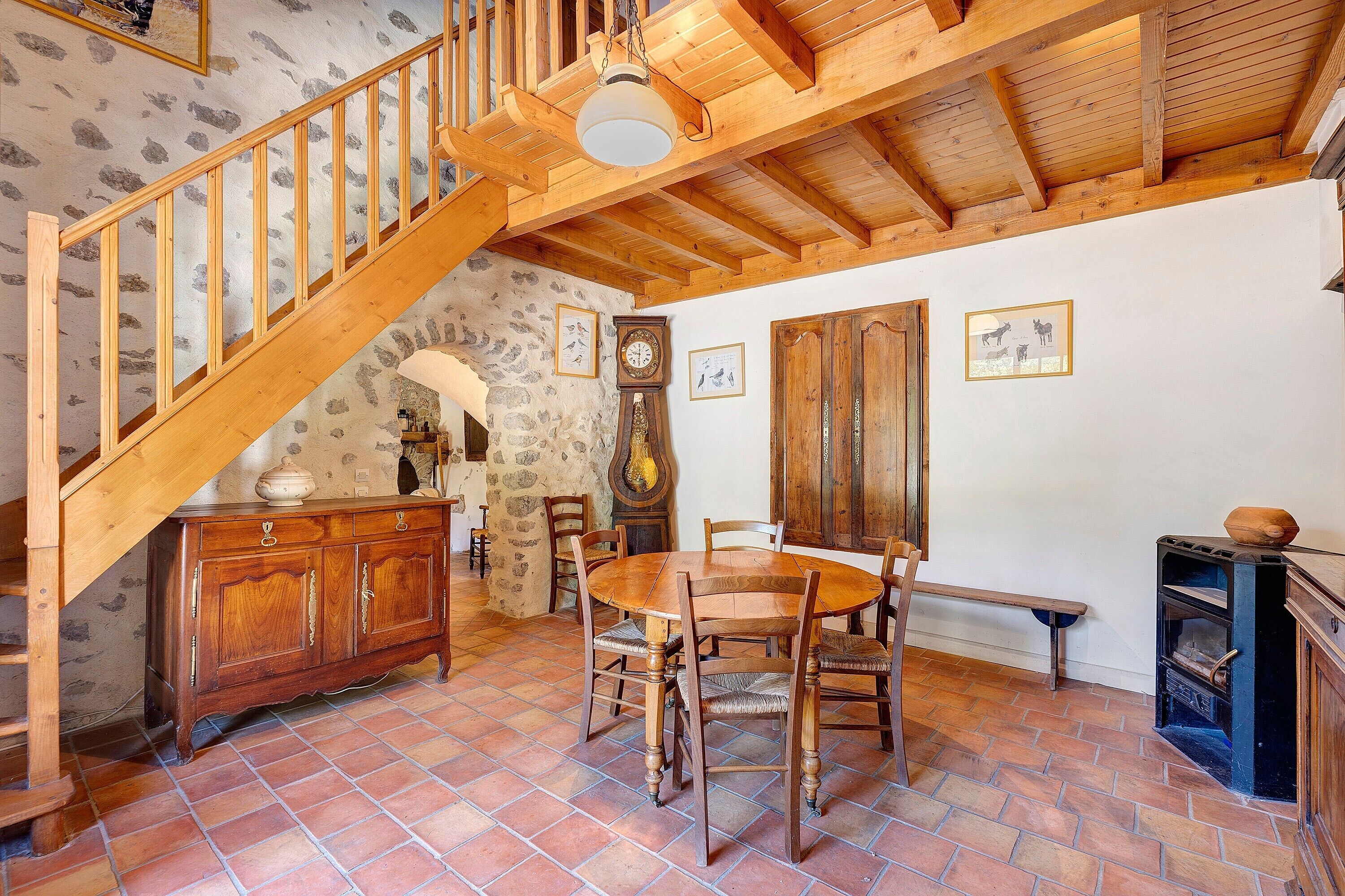 Ein rustikaler Innenraum mit einer Holztreppe, einem Esstisch mit Stühlen, einem Holzkabinett und einem Kamin.