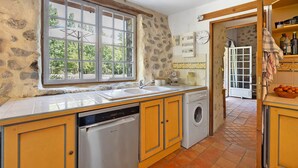A kitchen with a stone wall, a window, a sink, a dishwasher, and a washing machine. - House in Provence in a Former Fulling Mill (Entrepierres)