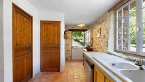 A kitchen with wooden doors, a large window, and a tiled floor. - House in Provence in a Former Fulling Mill (Entrepierres)