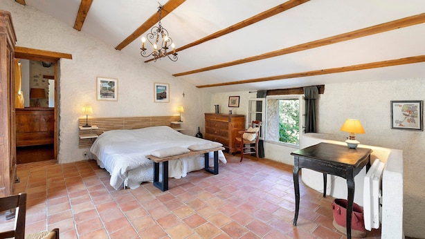 A bedroom with a wooden bed, a desk, and a chair. There is a window with curtains, a chandelier, and a wall with framed pictures. - House in Provence in a Former Fulling Mill (Entrepierres)