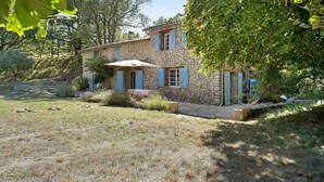 A stone house with a tiled roof, blue shutters, and a covered patio area. - House in Provence in a Former Fulling Mill (Entrepierres)