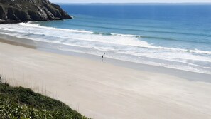 Una playa con una persona caminando por la orilla, un acantilado rocoso y el océano.