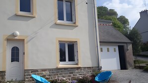 Une maison à deux étages avec une porte d’entrée, deux fenêtres et un petit garage attenant.