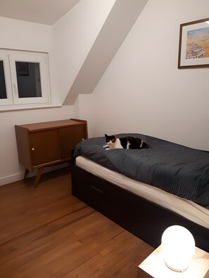 Un dormitorio con una cama, un aparador de madera, una ventana y una lámpara fijada a la pared.