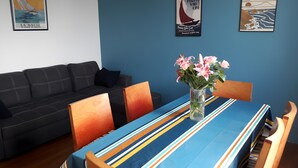 Un coin repas avec une table dressée pour deux personnes, un vase de fleurs et une nappe à rayures bleues.