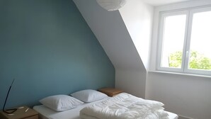 Une chambre à coucher avec un lit, une table de chevet, une lampe, une fenêtre et un plafond en pente.