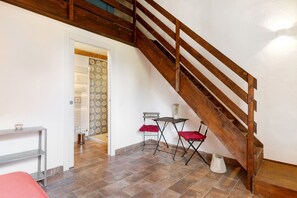 Una escalera con barandillas de madera, una pequeña mesa con un cojín rojo y un estante metálico.