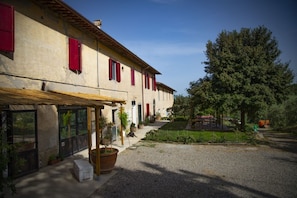Un bâtiment avec une allée gravillonnée, un patio couvert et un grand arbre en arrière-plan.