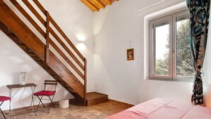 Slaapkamer met een houten trap, een raam met uitzicht, een bed en een kleine tafel met stoelen.