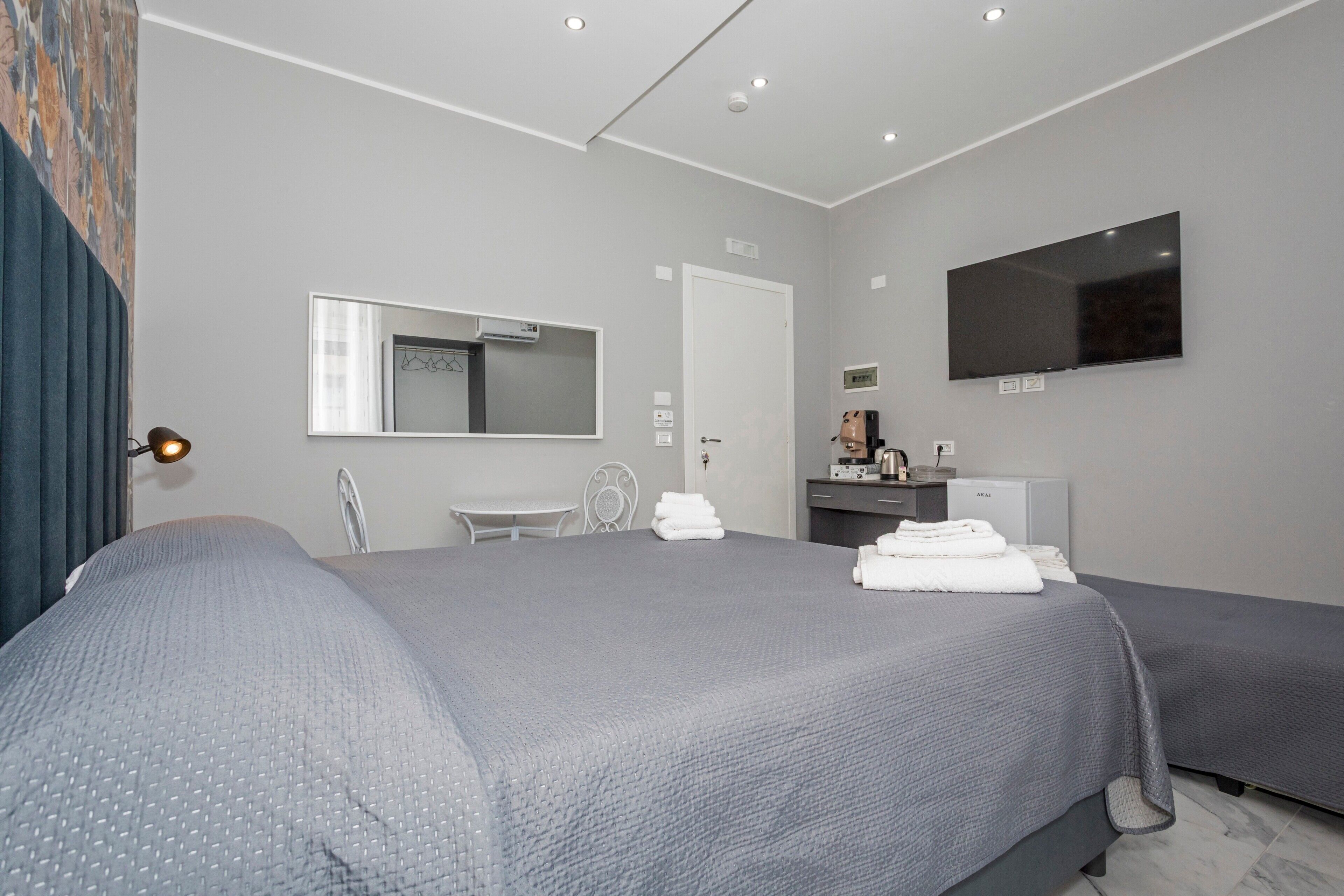 A modern hotel room with a large bed, a desk with a flat-screen TV, a mirror, and a door.