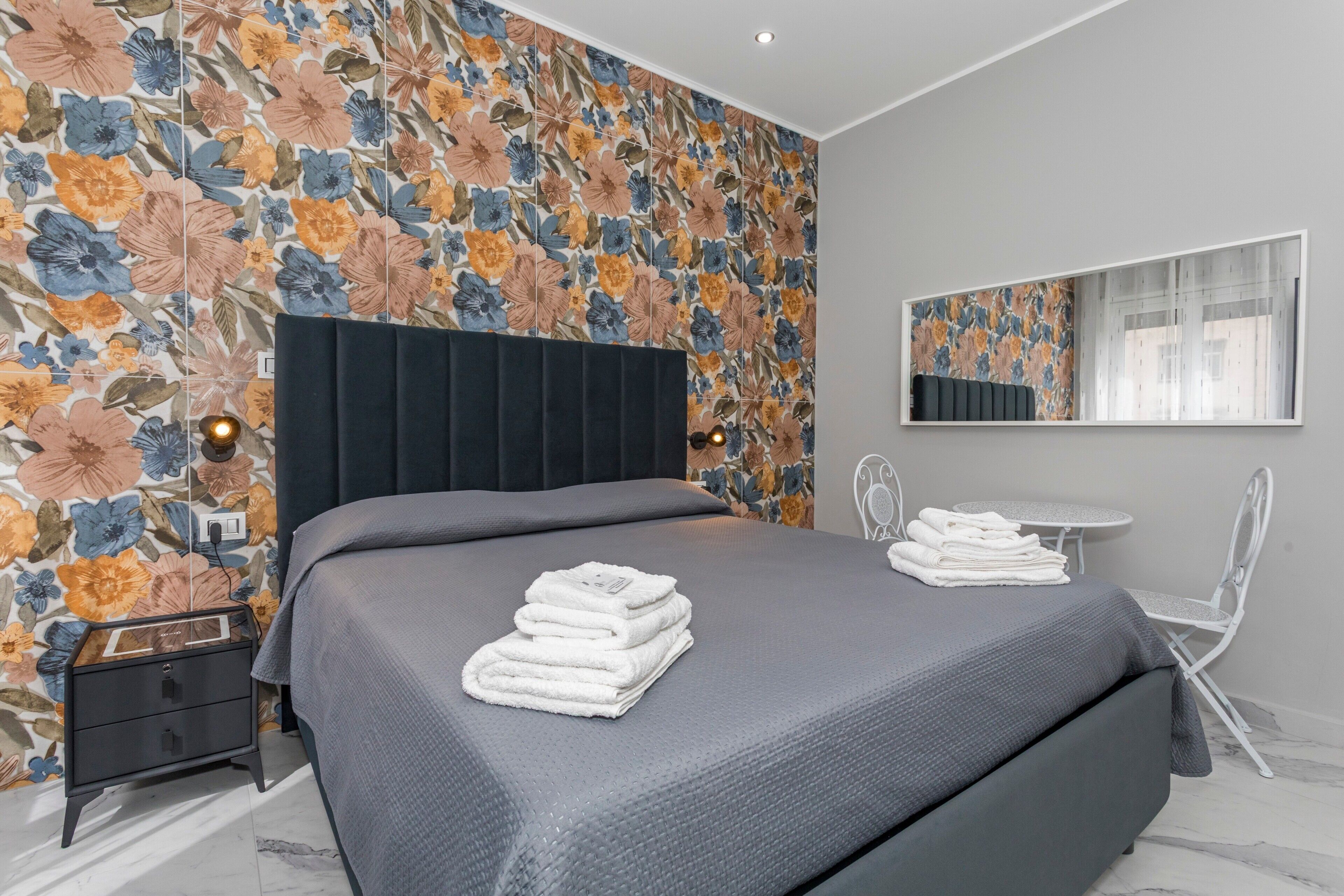 Ein Schlafzimmer mit einem Bett, einem Nachttisch, einem Stuhl, einem Tisch und einem Spiegel.