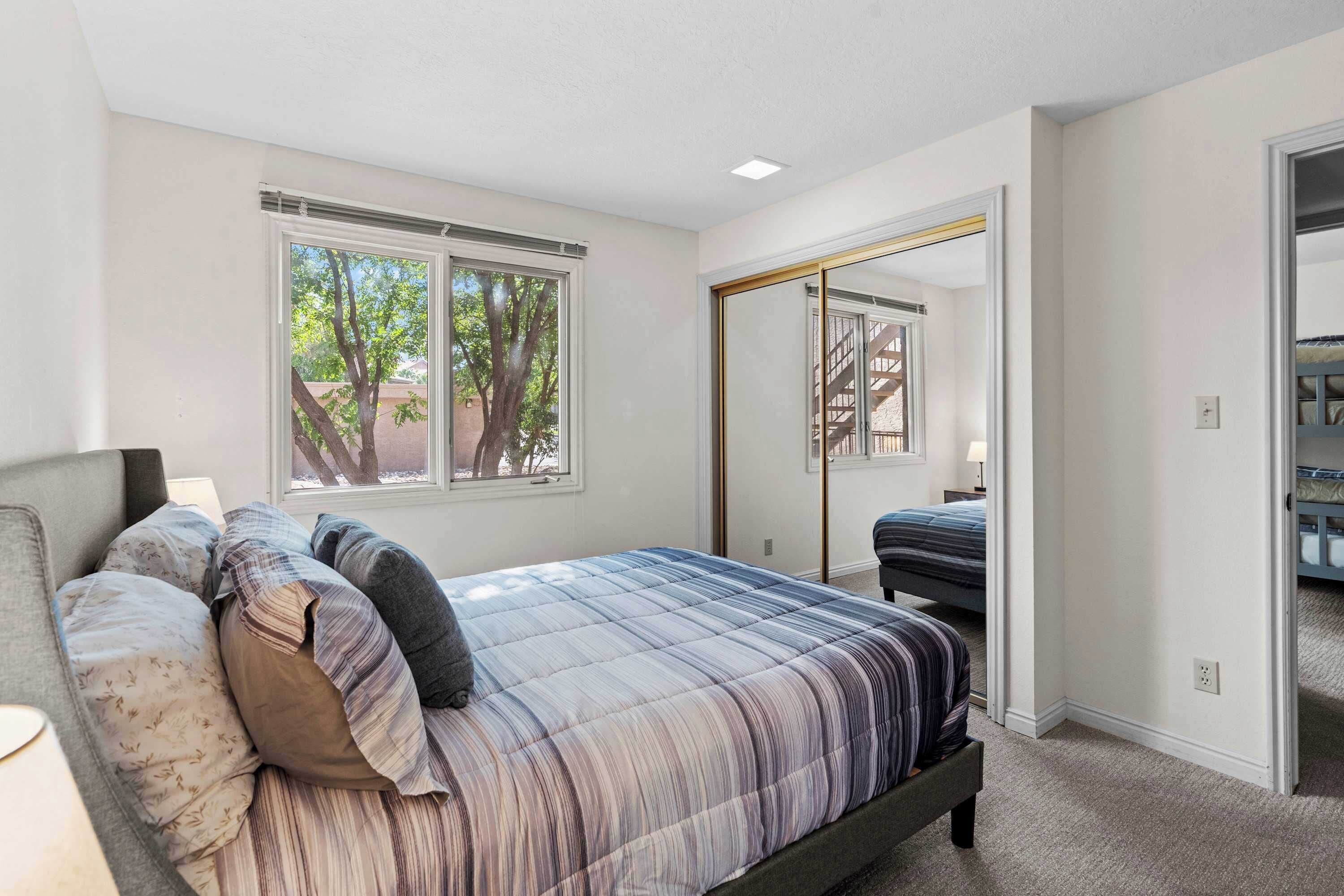 A bedroom with a bed, a window, a door, and a view of trees outside.