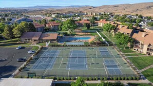 Vista aérea de una zona residencial con una gran cancha de tenis, rodeada de casas y una cadena montañosa al fondo.