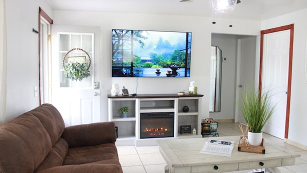 Una sala de estar con un sofá marrón, una chimenea, un televisor de pantalla plana y una mesa de centro con una planta.