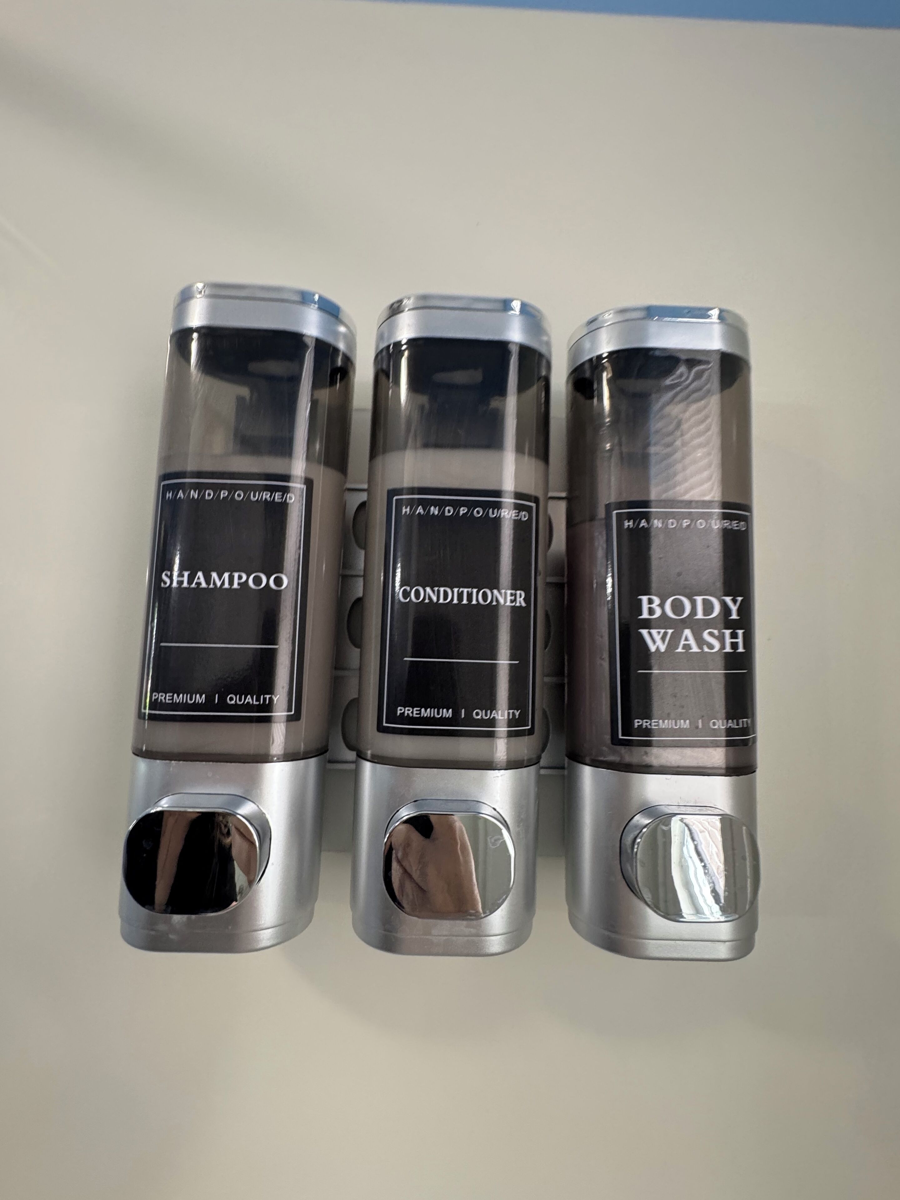 Trois récipients cylindriques étiquetés pour le shampoing, l’après-shampoing et le gel douche.