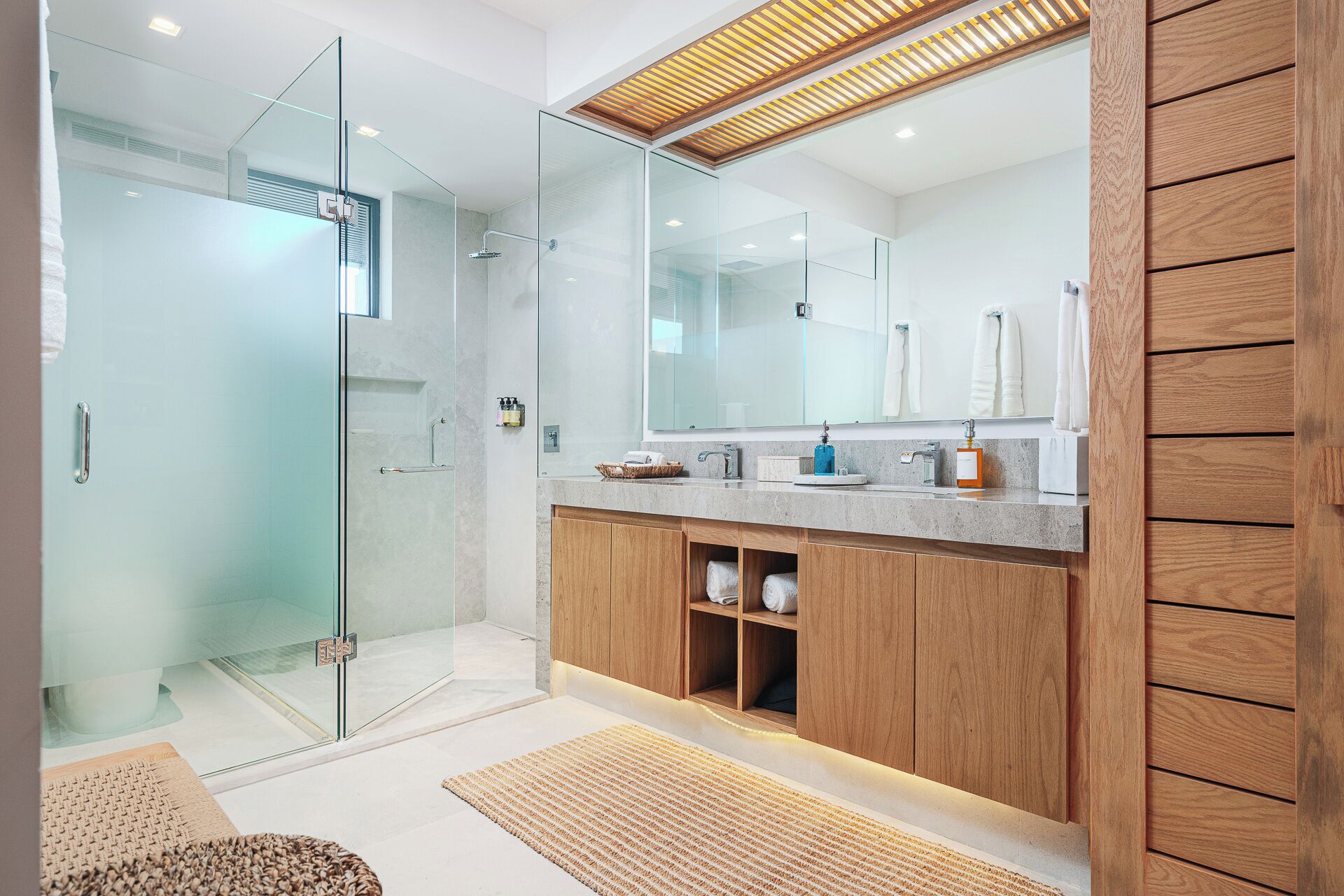 Une salle de bain moderne avec une douche à parois de verre, un grand miroir, des meubles en bois et un plan de toilette en marbre.