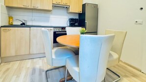 A compact kitchen with light wooden cabinets, a stainless steel refrigerator, a round wooden table, and white chairs. - Cozy Private Room | Shared Flat Near FAC Platz (Vienna)