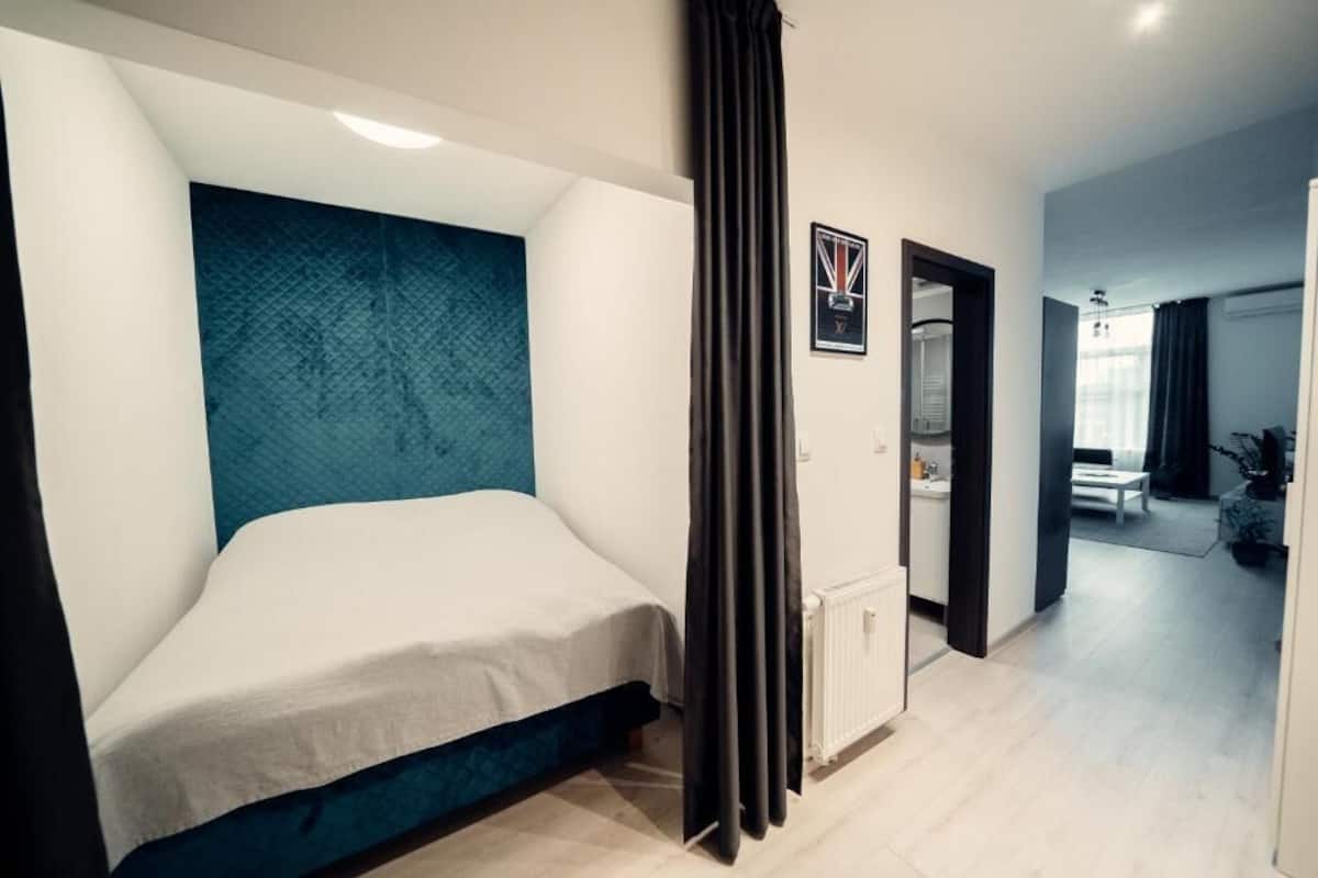 Une chambre d’hôtel moderne avec un lit simple, une grande fenêtre et vue sur le couloir.