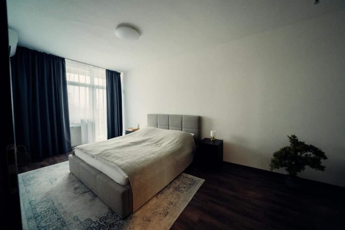Une chambre à coucher avec un lit, une table de chevet, une plante en pot et une fenêtre avec des rideaux.